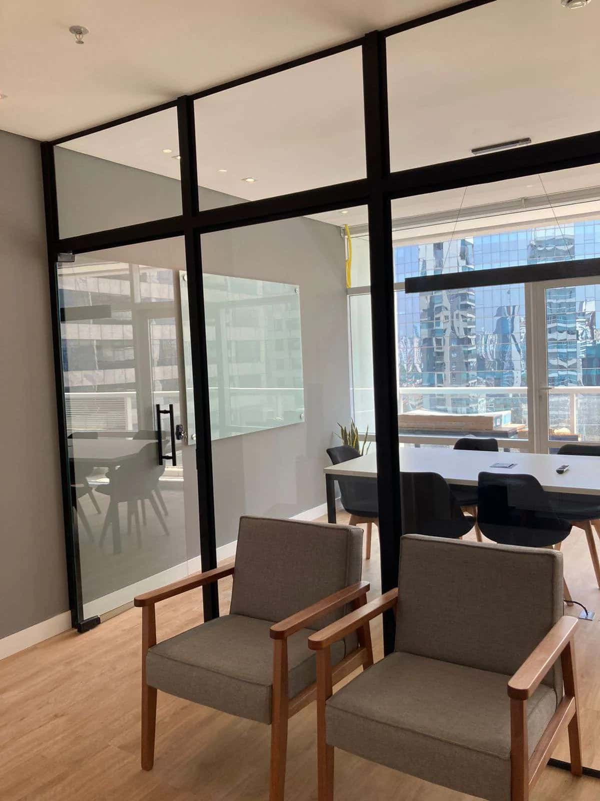 Sala de reunião com paredes de vidro e vista para os prédios da cidade
