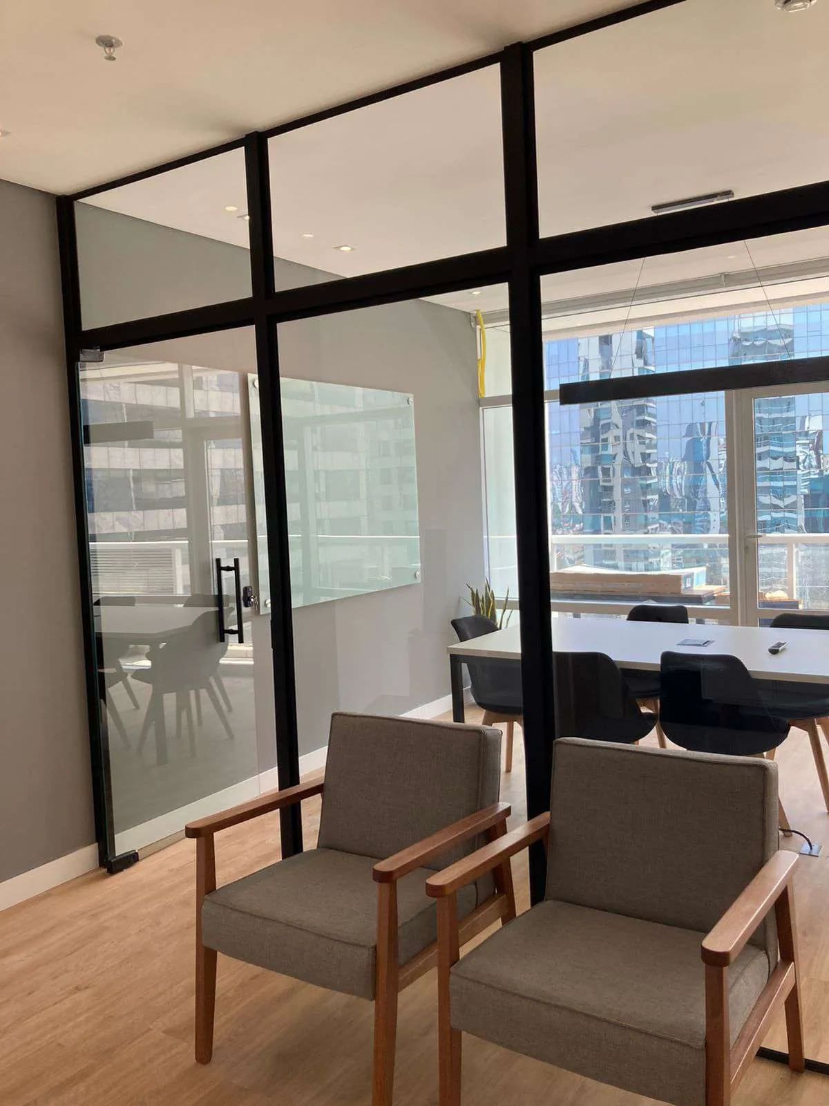 Sala de reunião com paredes de vidro e vista para os prédios da cidade