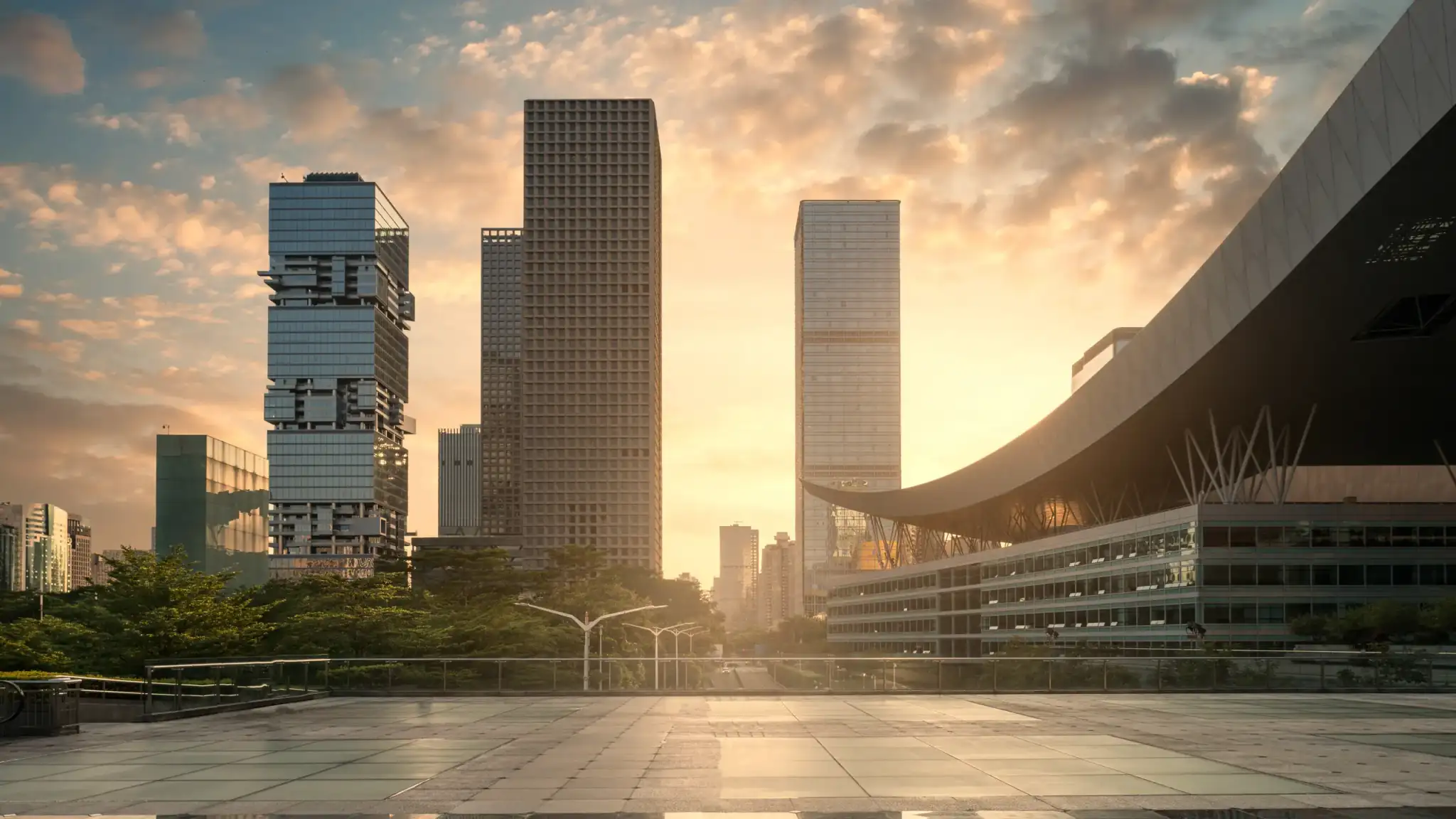 Torres corporativas ao pôr do sol vistas de uma praça, com um edifício de cobertura curva à direita