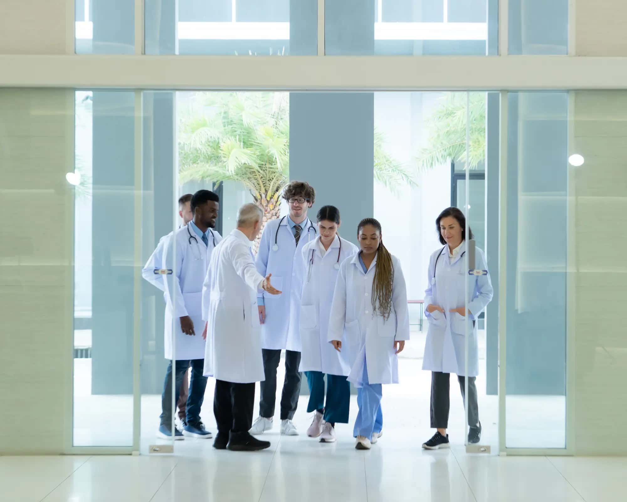 A medical team in white coats gathered at a hospital's glass entrance